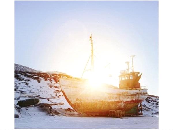 Photographie d'un bateau sur le rivage dans un paysage hivernal, le soleil se couche en arrière plan
