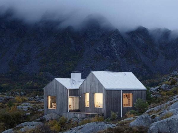 Photographie d'une maison au style scandinave, il y a de la lumière à l'intérieur, c'est la tombée de la nuit, il y a du brouillard