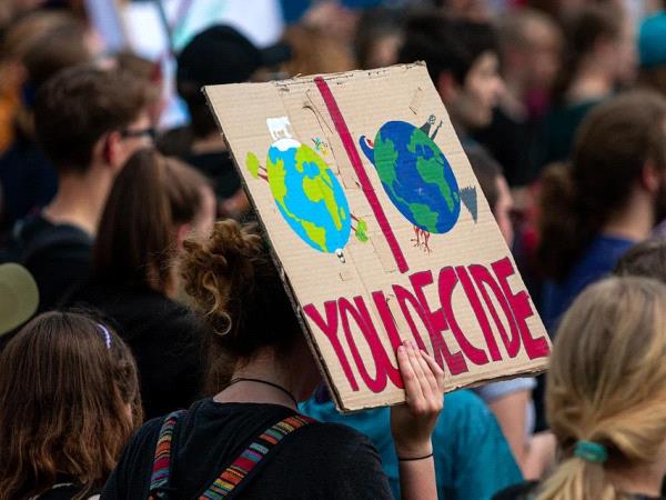 Photographie d'une manifestation, on voit une pancarte avec marqué dessus "you decide" ainsi que deux globes terrestres : un vert terne et l'autre vert vif